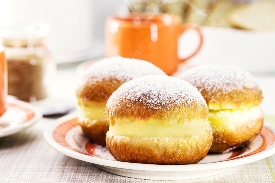 Sonhos dourados com creme amarelo e açúcar em prato para café da manhã