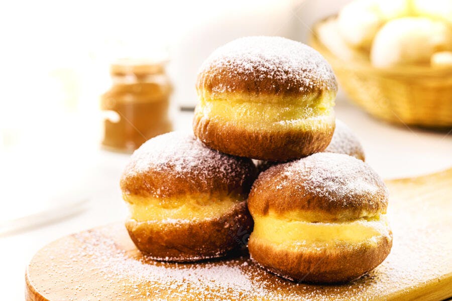 Sonhos doces recheados com creme e açúcar em tábua de madeira clara