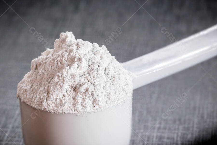 Pó de proteína branco em colher medidora sobre fundo cinza