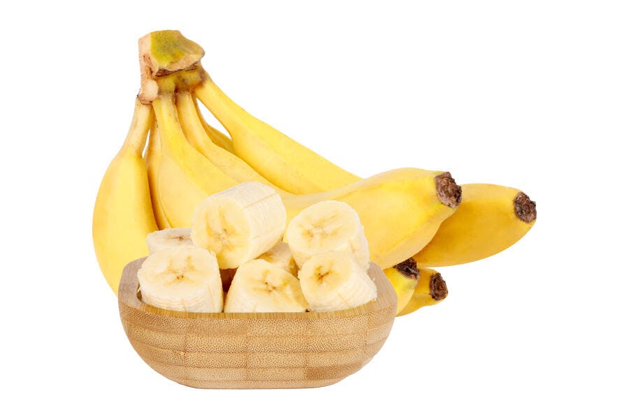 Cacho de bananas amarelas e fatias em tigela de madeira