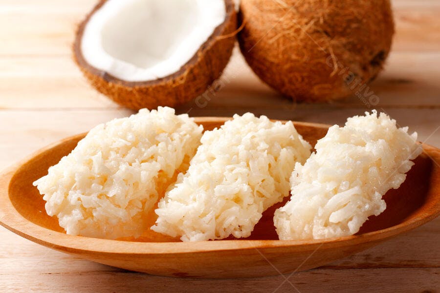 Cocada de coco doce brasileiro em tigela de madeira com cocos frescos