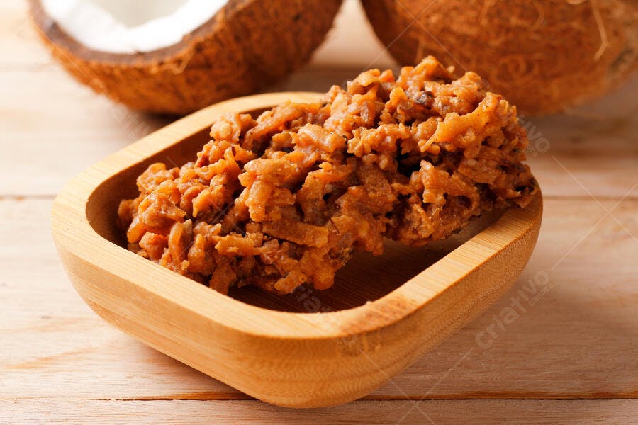 Cocada de coco caramelizada em tigela de madeira rústica com cocos frescos