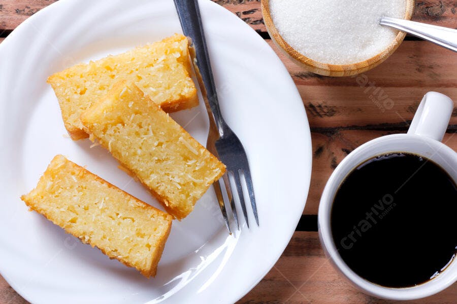 Fatias de bolo de coco amarelo fresco com café e açúcar em mesa de madeira