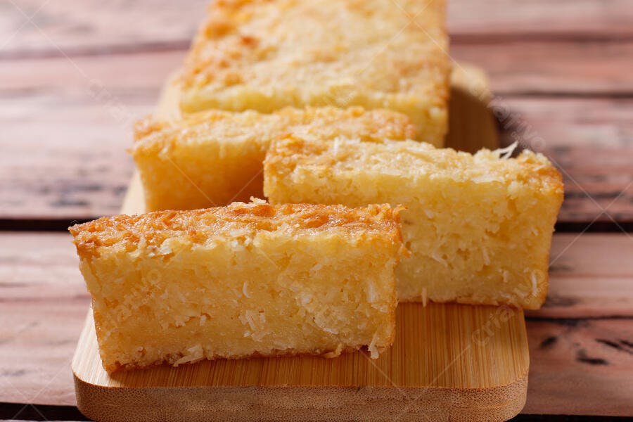 Bolo de coco cremoso fatiado em tábua de madeira com cobertura dourada