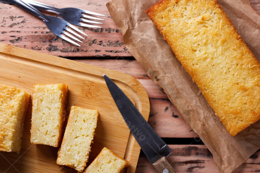 Bolo de coco fatiado na tábua de madeira rústica com faca e garfos sobre mesa