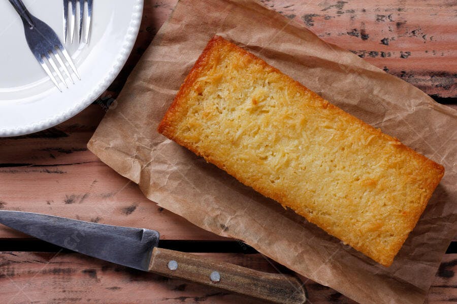 Bolo de coco dourado em papel pardo na mesa de madeira com talheres rústicos