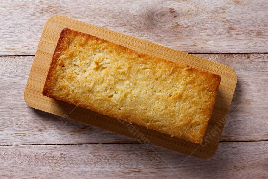 Bolo de coco retangular dourado em tábua de madeira clara