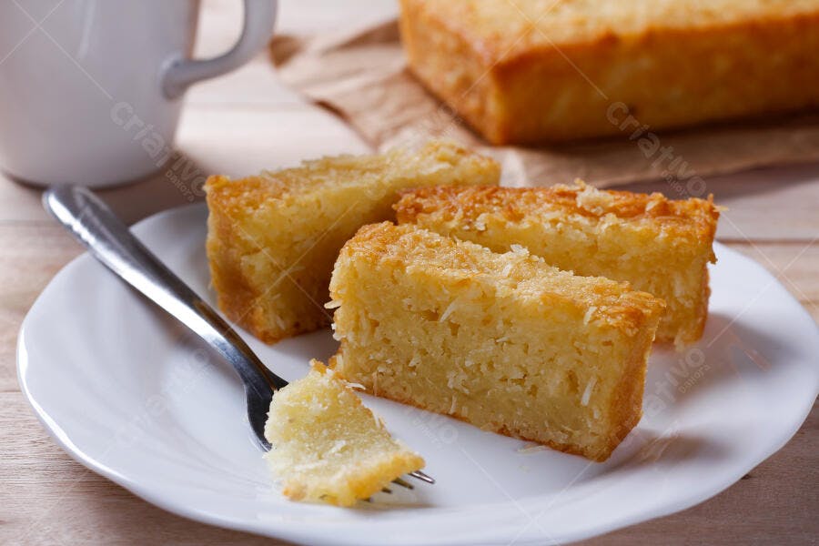 Bolo de coco fatiado em prato branco com garfo e xícara de café