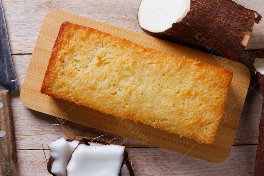 Bolo de mandioca dourado na tábua de madeira com coco e raiz de mandioca