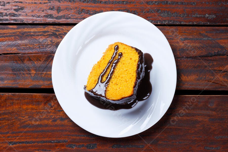 Bolo de cenoura fatia individual com calda de chocolate em prato branco e mesa de madeira