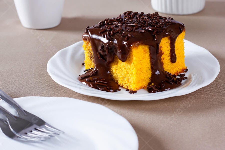 Bolo de cenoura laranja com cobertura de chocolate e granulado em prato branco