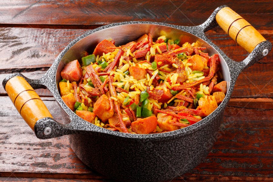 Arroz de carreteiro na panela rústica com carne seca e pimentão verde em mesa de madeira