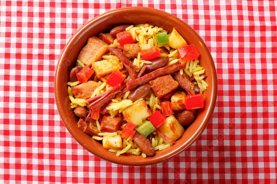 Arroz colorido com carne feijão pimentões em tigela de barro sobre toalha xadrez