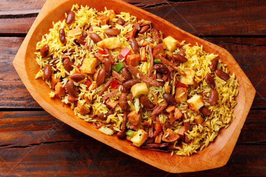Prato de arroz amarelo com feijão vermelho e carne desfiada em tigela de madeira