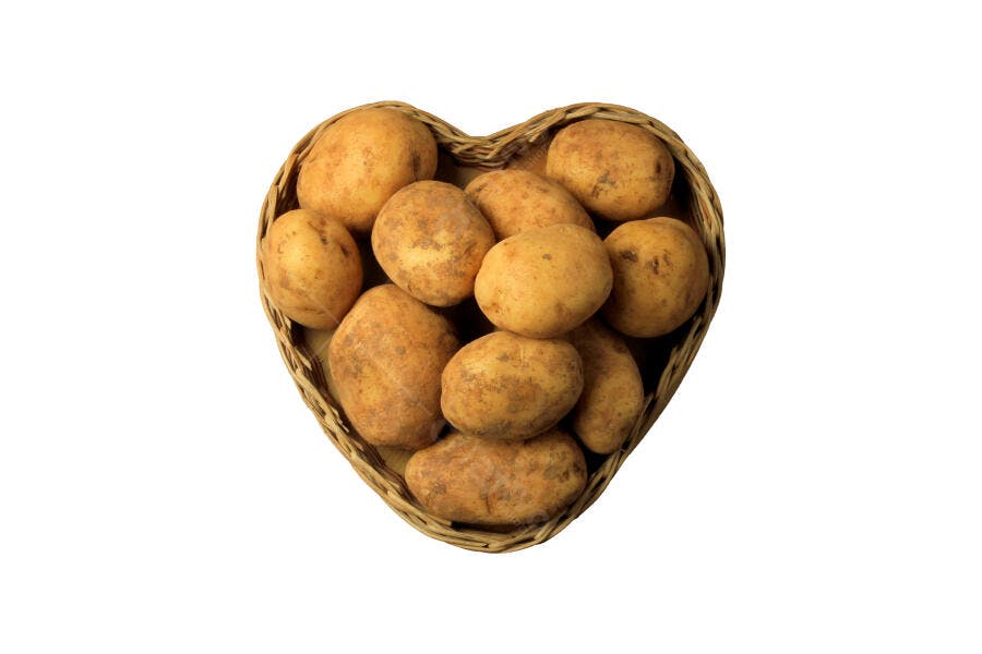 Batatas cruas em cesta de vime formato coração em fundo branco