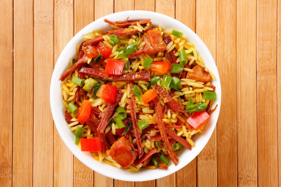 Prato de arroz com carne seca pimentões e cebolinha em mesa de madeira
