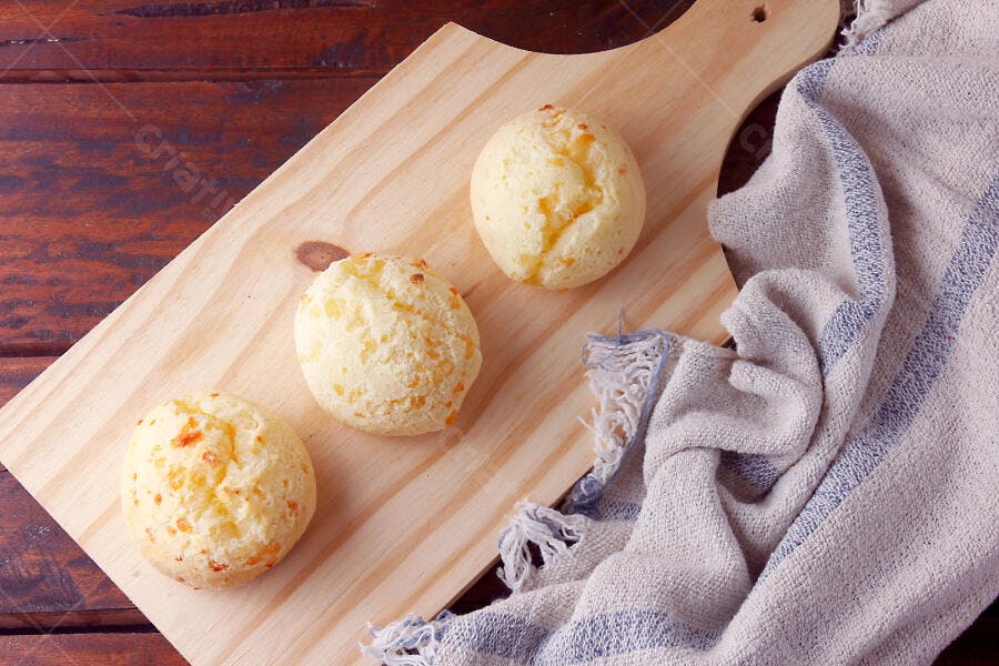 Pães de queijo frescos em tábua de madeira com pano de prato rústico