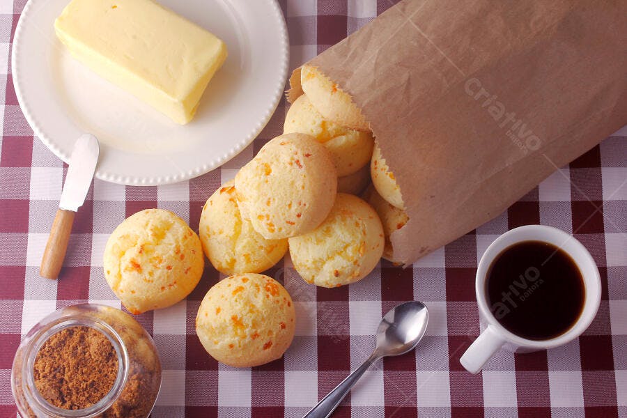 Pão de queijo recém-assado com café e manteiga em mesa xadrez vermelha
