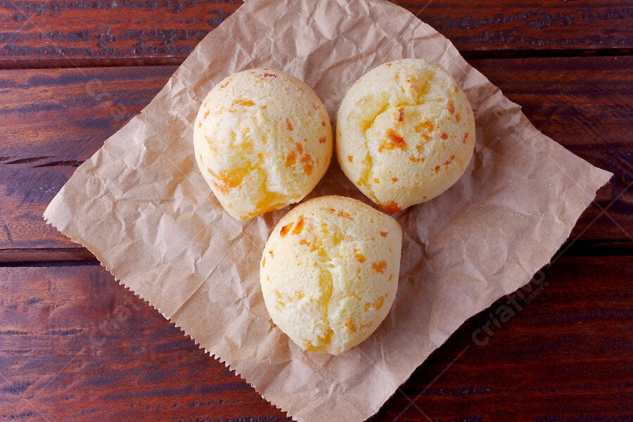 Três pães de queijo em papel manteiga sobre mesa de madeira escura