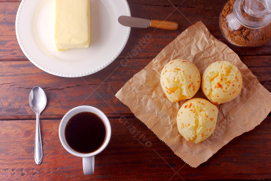 Pão de queijo fresco com café e manteiga em mesa rústica de madeira