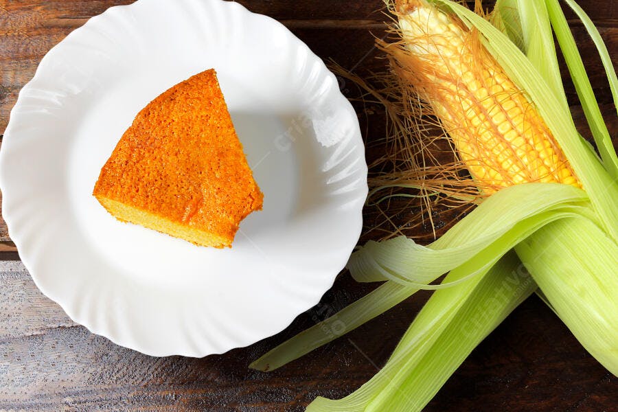 Bolo de milho cremoso em prato branco com espiga fresca em mesa rústica