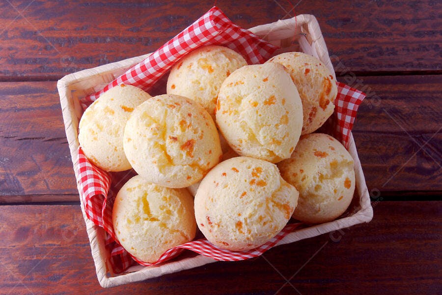 Pão de queijo cremoso em cesto com toalha xadrez sobre madeira escura