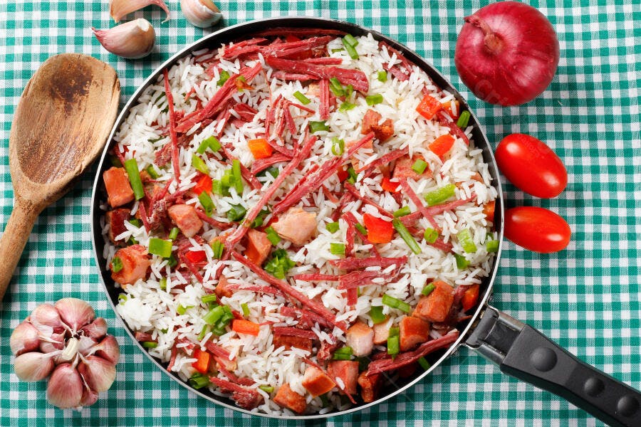 Prato de arroz com carne desfiada e legumes na panela sobre toalha verde