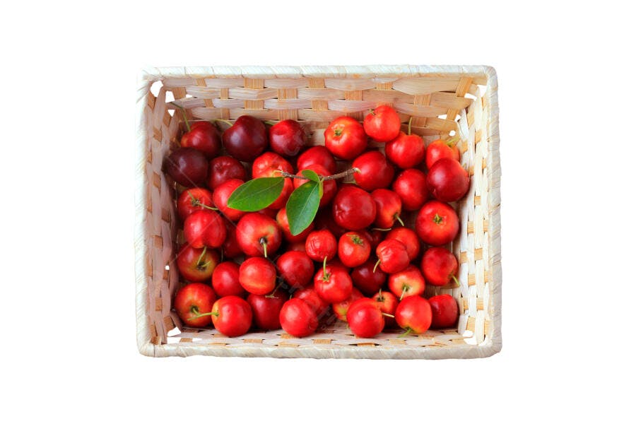 Acerolas frescas vermelhas em cesta de palha com folhas verdes fundo branco