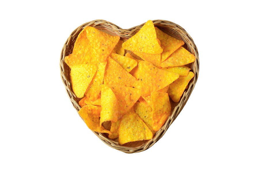 Tortilla chips amarelos crocantes em cesta de coração com fundo branco