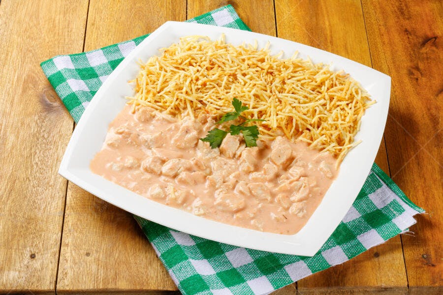 Strogonoff de frango cremoso com batata palha e salsa em prato branco