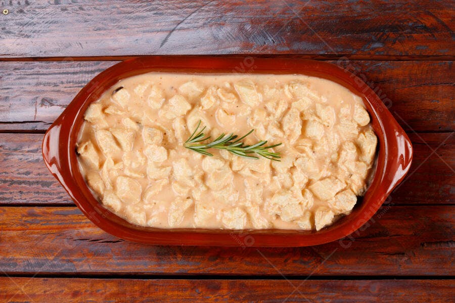 Frango cremoso em travessa de barro com alecrim em mesa rústica de madeira