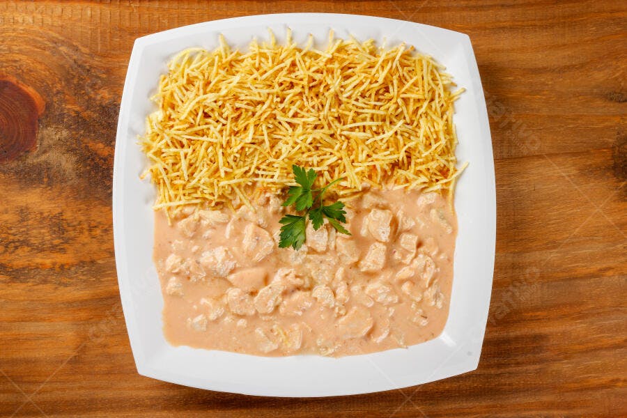 Prato de estrogonofe de frango com batata palha e salsa fresca em mesa rústica de madeira