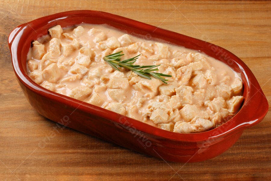 Frango cremoso em travessa vermelha com alecrim sobre mesa de madeira