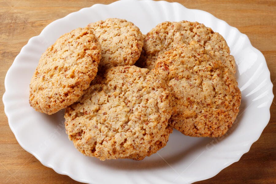 Biscoitos de amêndoas crocantes em prato branco sobre mesa de madeira