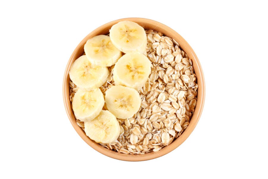 Tigela de aveia com fatias de banana fresca em fundo branco vista superior
