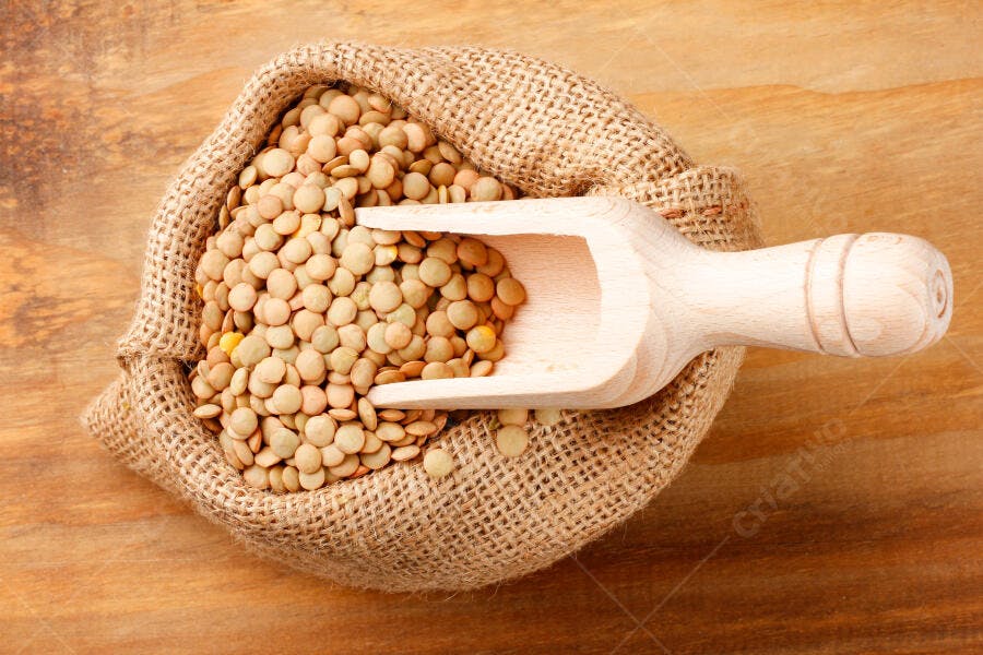 Lentilhas marrons em saco de estopa com colher de madeira em fundo rústico