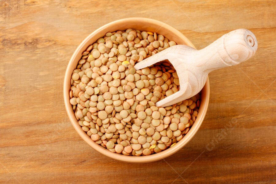 Tigela de lentilha crua com colher de pau em mesa de madeira
