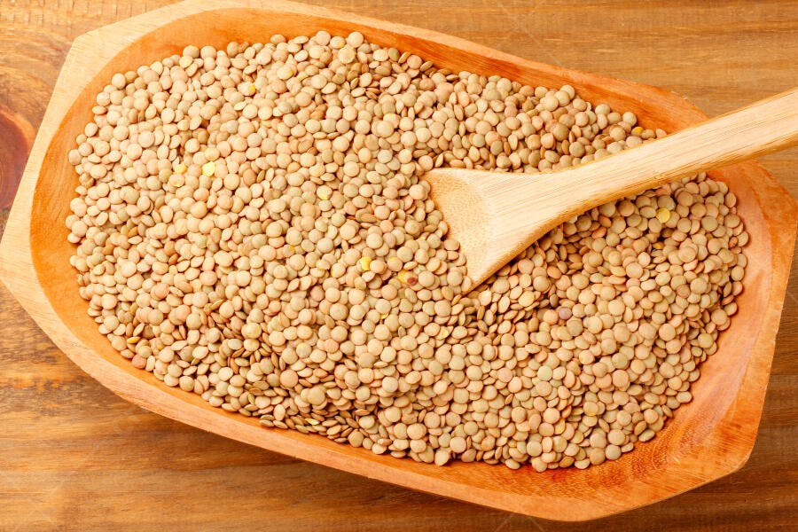 Lentilhas marrom-esverdeadas em tigela de madeira com colher de bambu