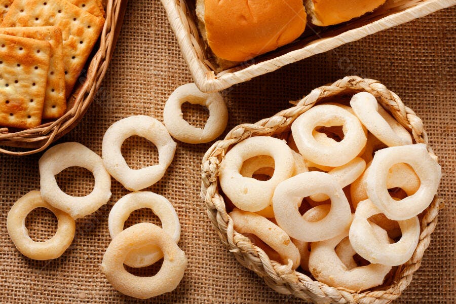Biscoitos de polvilho cream cracker e pães frescos em cestas com fundo rústico de juta