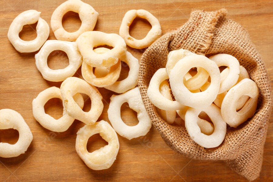 Biscoitos de polvilho brancos e crocantes em saco de aniagem rústico na mesa de madeira