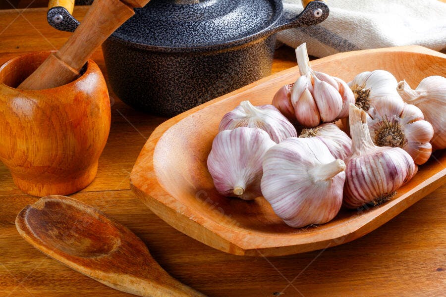 Alho roxo fresco em tigela de madeira com pilão e panela rústica