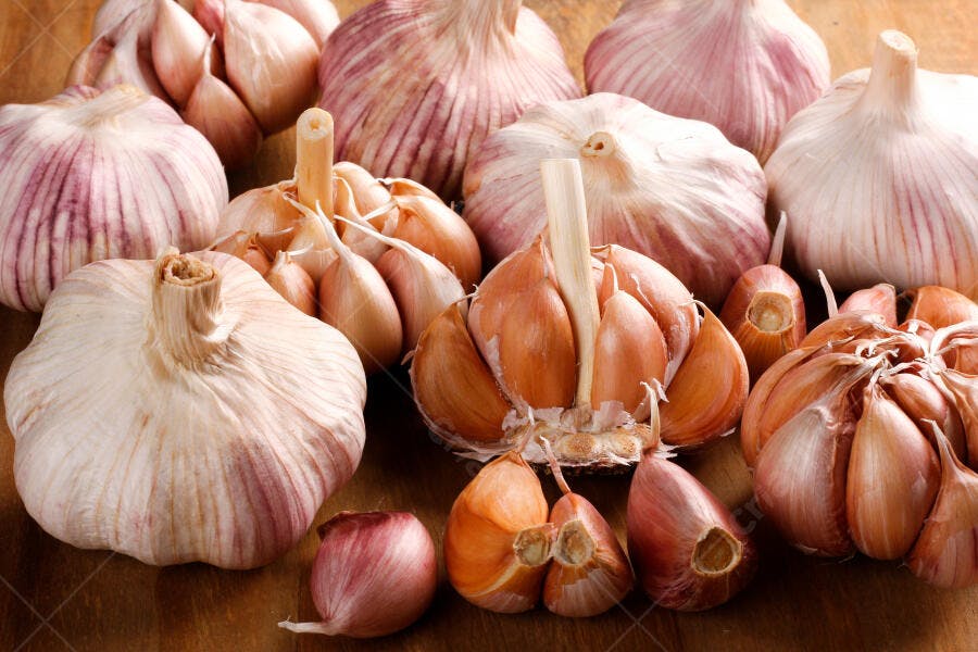 Bulbos de alho brancos e roxos com dentes espalhados em madeira rústica
