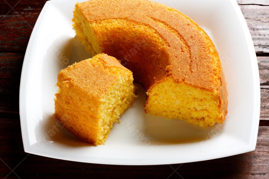 Bolo de milho fofo amarelo com fatia em prato branco sobre mesa de madeira rústica