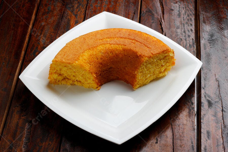 Bolo de milho caseiro em prato branco sobre mesa rústica de madeira