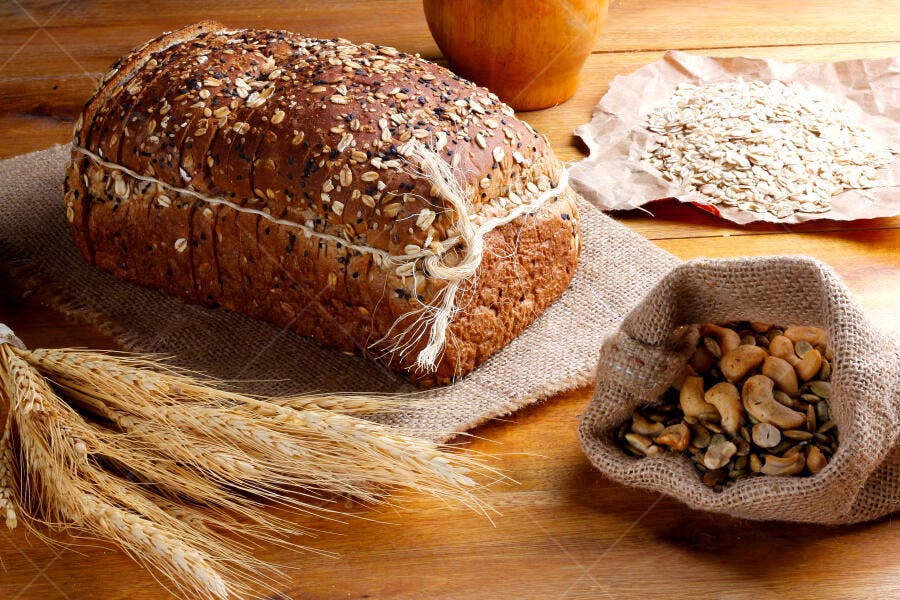 Pão integral fatiado com grãos e aveia sobre mesa de madeira rústica