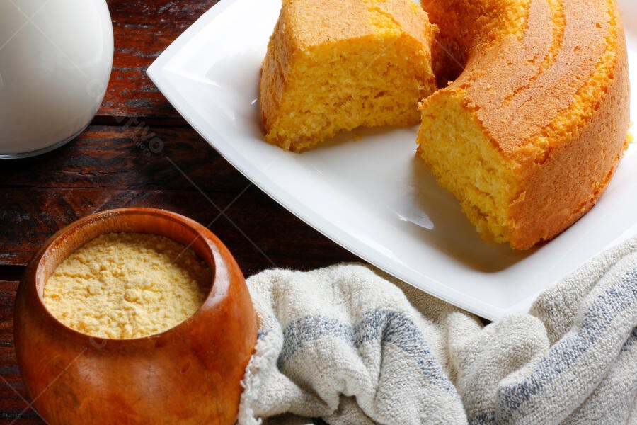 Bolo de fubá dourado em prato branco com fubá e leite em mesa rústica de madeira