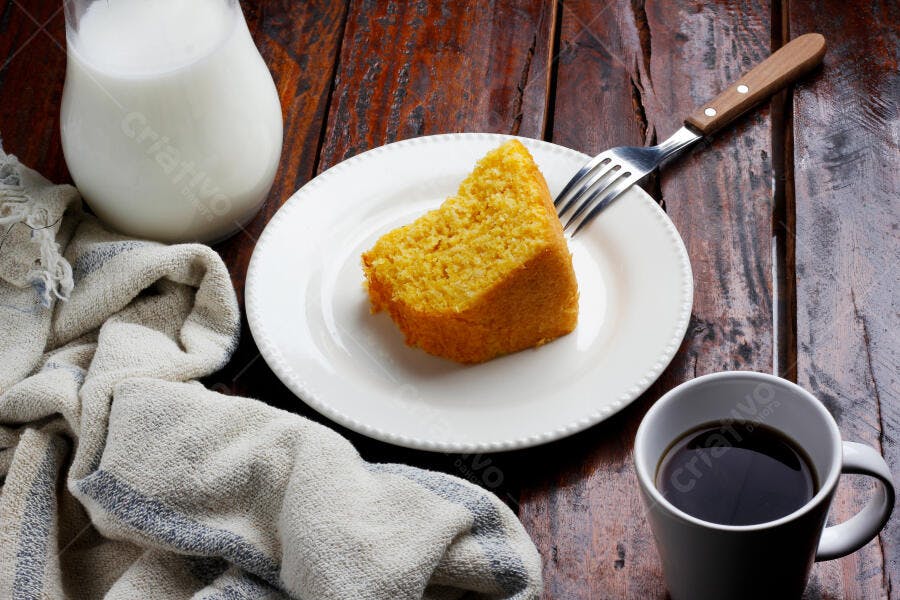 Fatia de bolo de milho amarelo em mesa de madeira rústica com café e leite