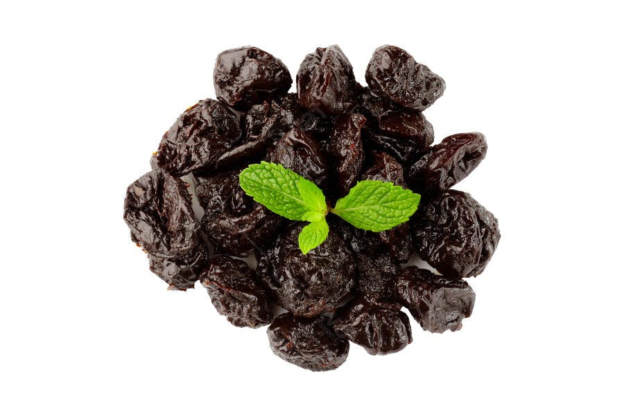 Ameixas secas marrons escuras com folhas de menta fresca em fundo branco