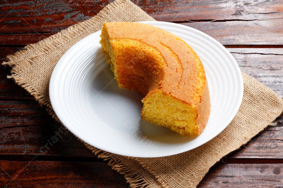 Bolo de fubá cremoso em prato branco sobre mesa rústica de madeira
