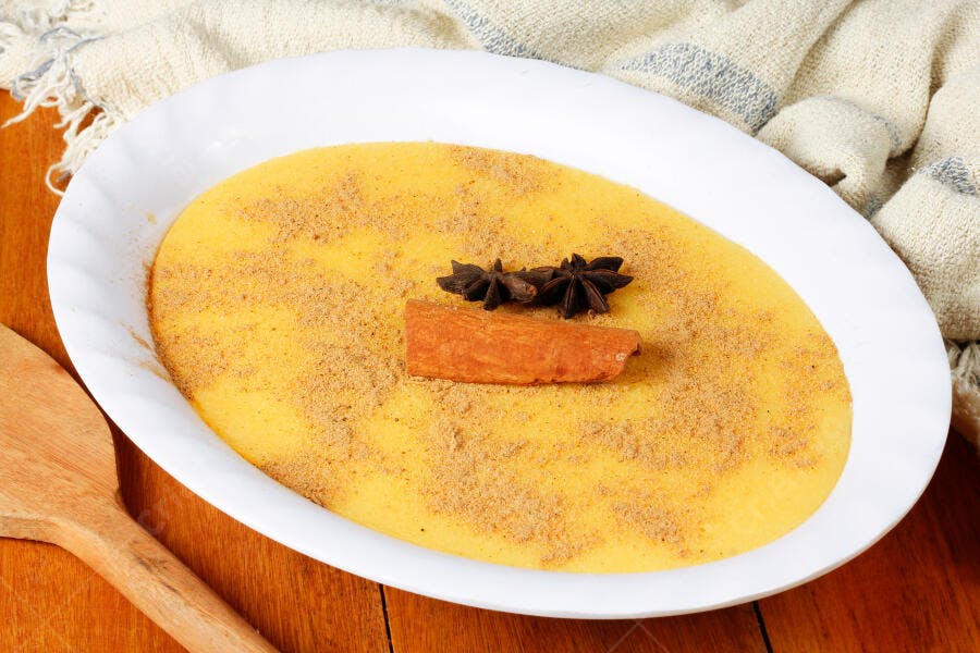 Curau de milho cremoso polvilhado com canela e anis estrelado em mesa de madeira